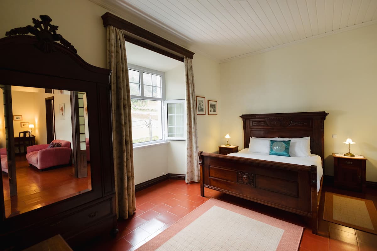 Un dormitorio con un espejo grande, cama de madera, mesitas de noche y una ventana con cortinas.