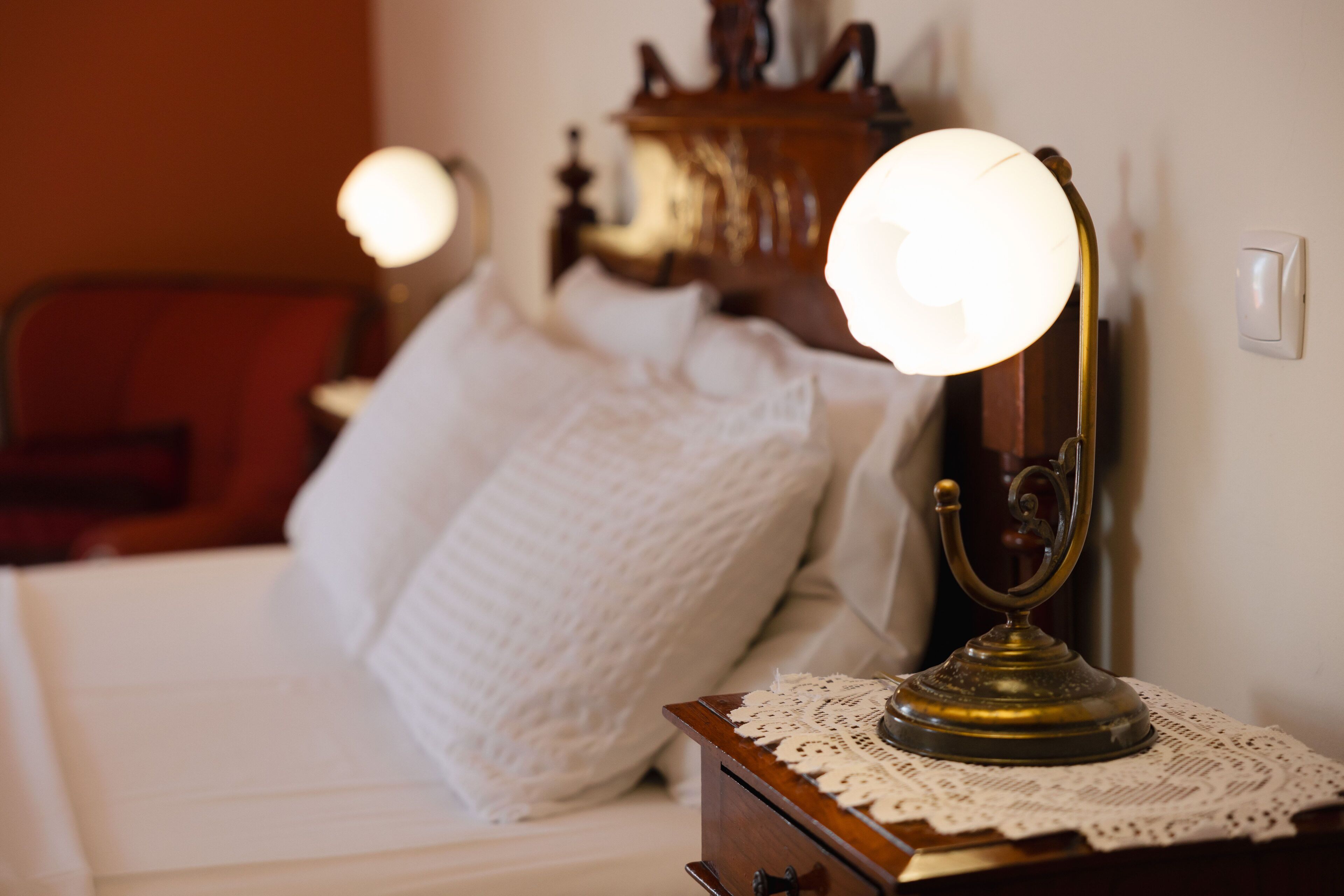 A neatly made bed with a white comforter and pillows, a wooden nightstand with a brass lamp, and a wooden dresser in the background.