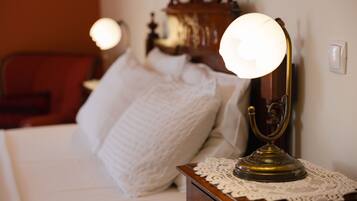 A neatly made bed with a white comforter and pillows, a wooden nightstand with a brass lamp, and a wooden dresser in the background.