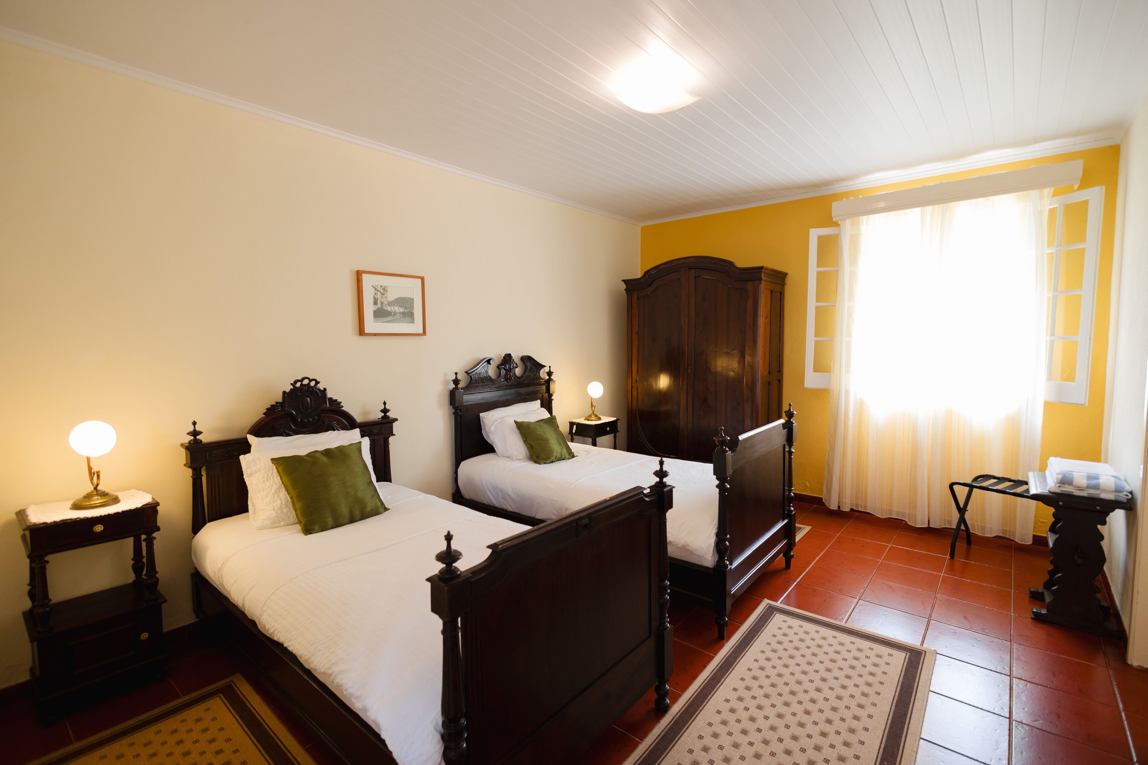 Una habitación con dos camas de madera, un armario de madera, una mesita y una ventana con cortinas.