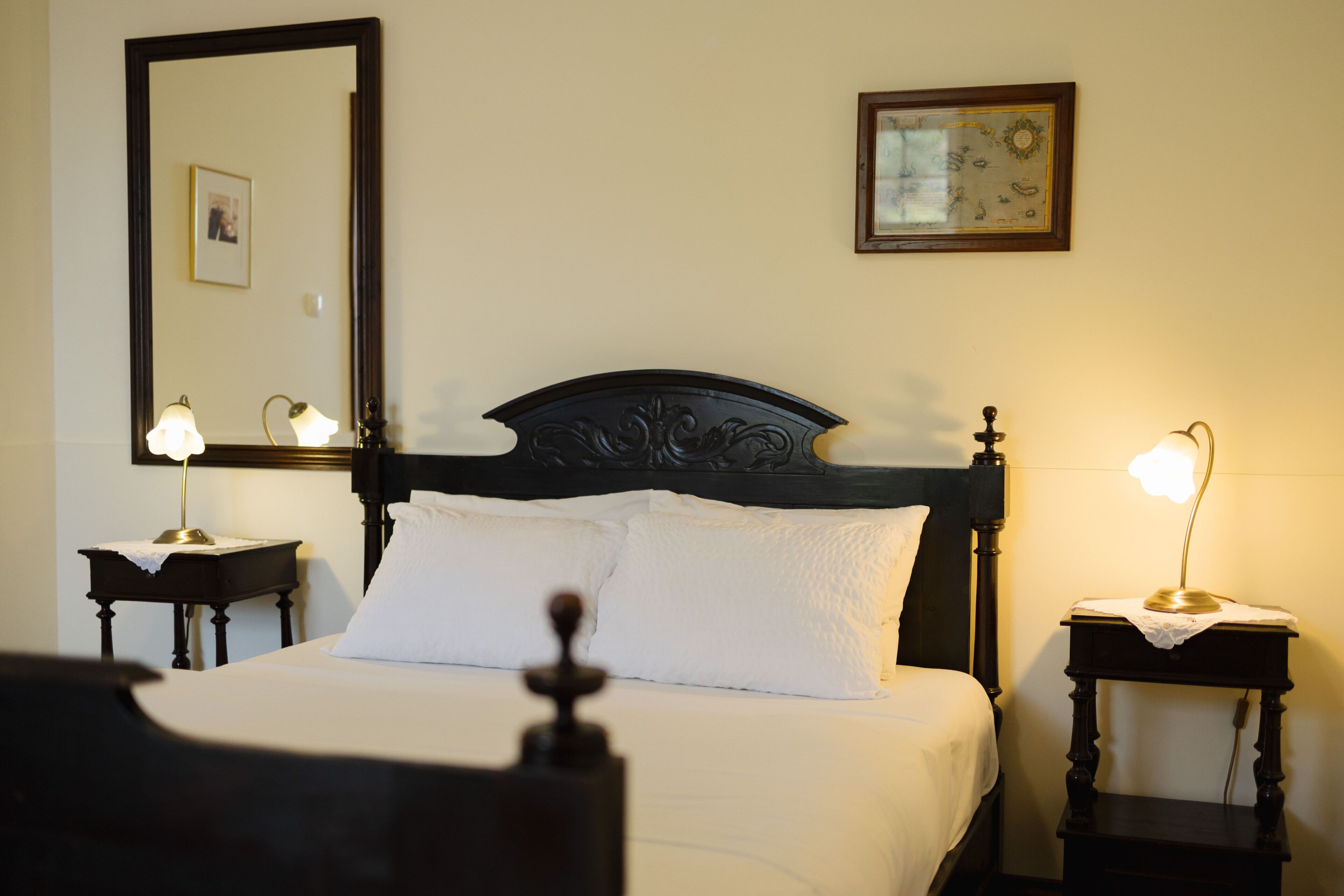 A neatly made bed with white linens, two bedside tables with lamps, a large mirror, and a framed picture on the wall.