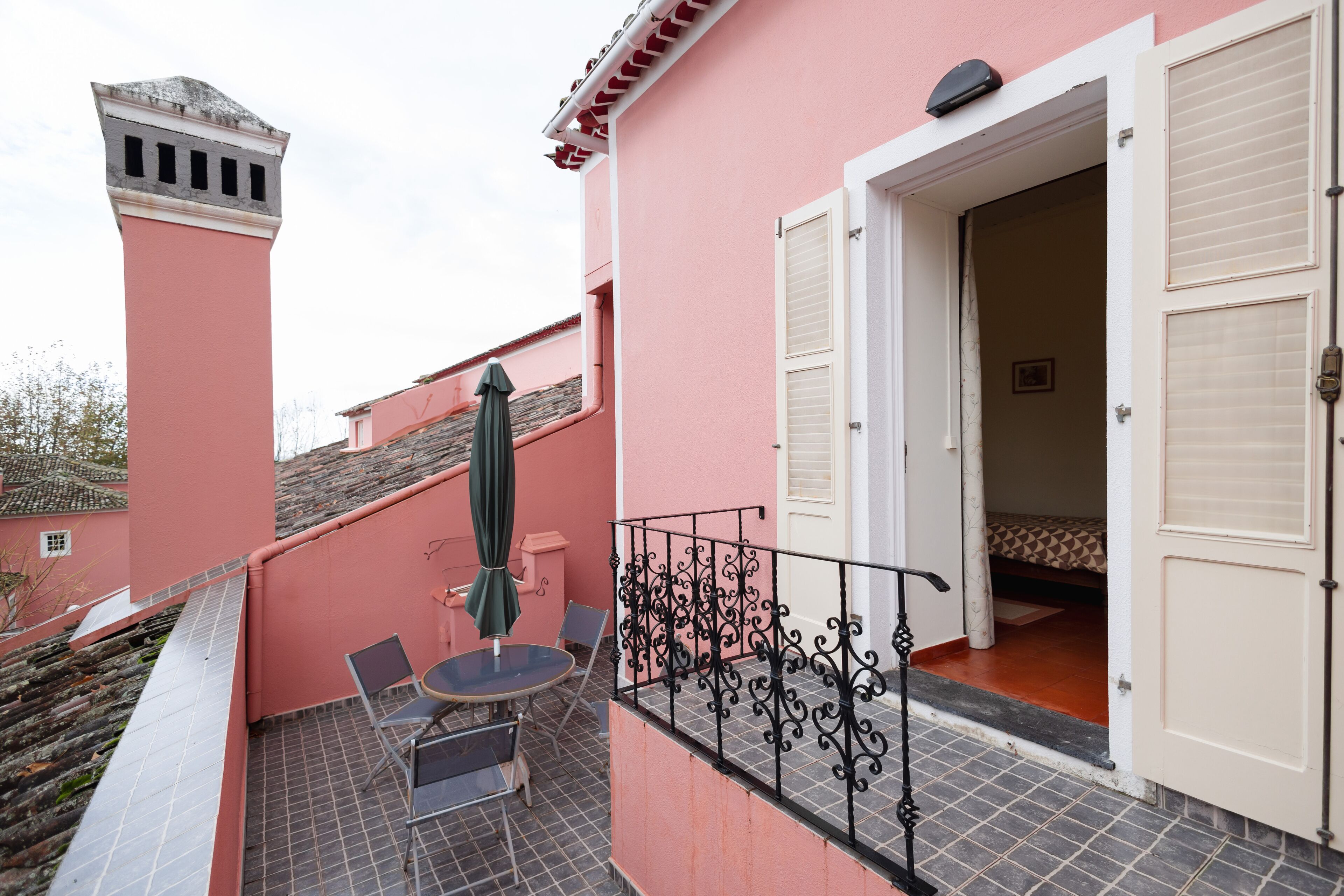 Un bâtiment rose avec un balcon, une table entourée de chaises et un parasol vert.