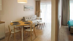 Una sala de estar moderna con una mesa de comedor redonda de madera, sillas blancas, un sofá beige y una pequeña mesa de centro blanca.