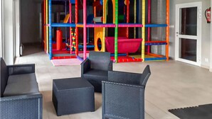 Zona de juegos con estructuras de escalada coloridas y un área de descanso con muebles de mimbre.