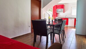 A dining area with a table set for two, a red accent wall, and a kitchen in the background. - Lovely home in Barbate with WiFi (Barbate)
