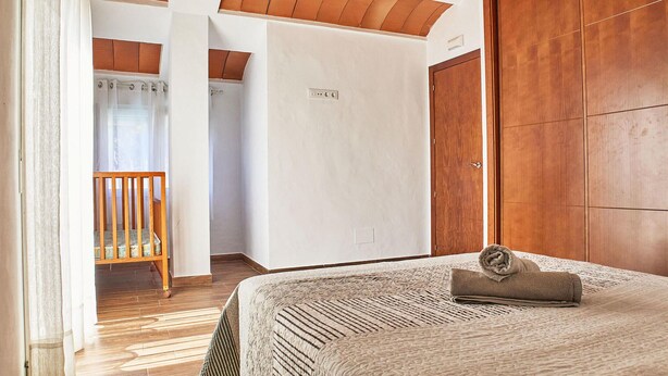 A bedroom with a wooden wardrobe, a bed with a rolled towel, a wooden chair, and a small table with items. - Lovely home in Barbate with WiFi (Barbate)