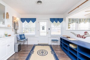 Ein Zimmer mit einer weißen Tür, blauen Vorhängen, einer blauen Bank, einem blauen Regal und einem Teppich mit Kompassmuster.