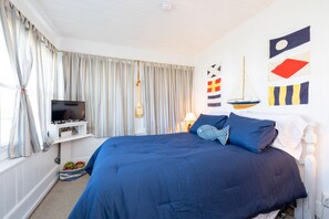 Ein Schlafzimmer mit einem großen Bett, einem Fernseher auf einem Regal, einer Bootsdekoration und maritimer Wandkunst.