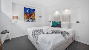 Een moderne hotelkamer met een groot bed, een schilderij aan de muur, een klein bijzettafeltje en een bedlampje.