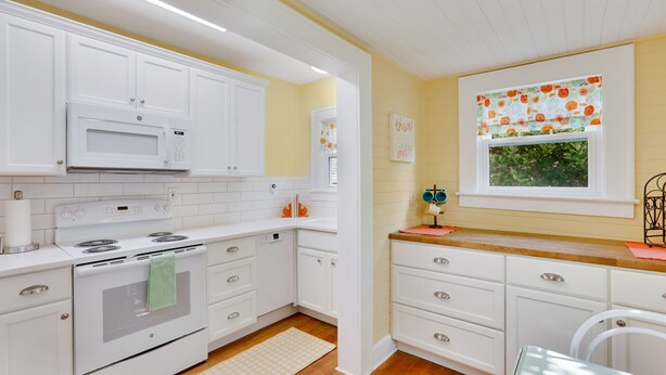 A kitchen with white cabinets, a microwave, stove, and a window with orange curtains. - Updated 1930s carriage house in Ardsley Park (Savannah)