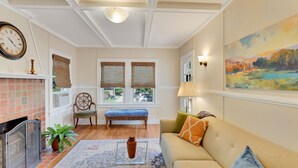 A cozy living room with a fireplace, a sofa, a bench, and a large window with blinds. - Updated 1930s carriage house in Ardsley Park (Savannah)