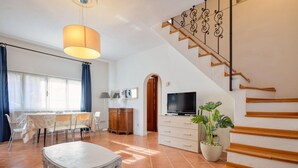 A spacious living area with a dining table, chairs, a TV, and a staircase.