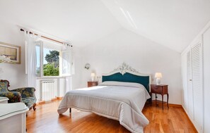 Een slaapkamer met een groot bed, een stoel, een nachtkastje, een raam met gordijnen en een radiator.