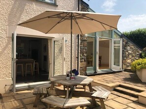 An outdoor patio with a round wooden table, benches, and a large umbrella.