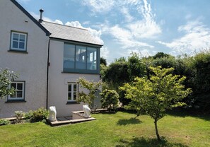 A two-story building with a large window, a chimney, and a well-maintained garden with a tree and shrubs.