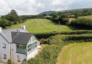 A house with a large window, a sloped roof, and a view of a green field and hills in the background. - Spectacular views over Newport Bay, Parrog, Nevern Estuary, and the Preseli Mountains (Newport)