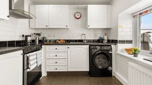 Une cuisine moderne avec des armoires blanches, une hotte de cuisinière en acier inoxydable, un four encastré, un lave-vaisselle et une fenêtre offrant une belle vue.