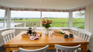 Une table à manger avec des chaises, un vase de fleurs et une vue sur un champ verdoyant par de grandes fenêtres.