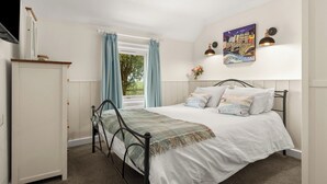 Une chambre à coucher avec un lit, une armoire, une fenêtre avec des rideaux, un tableau au mur et un luminaire au plafond.