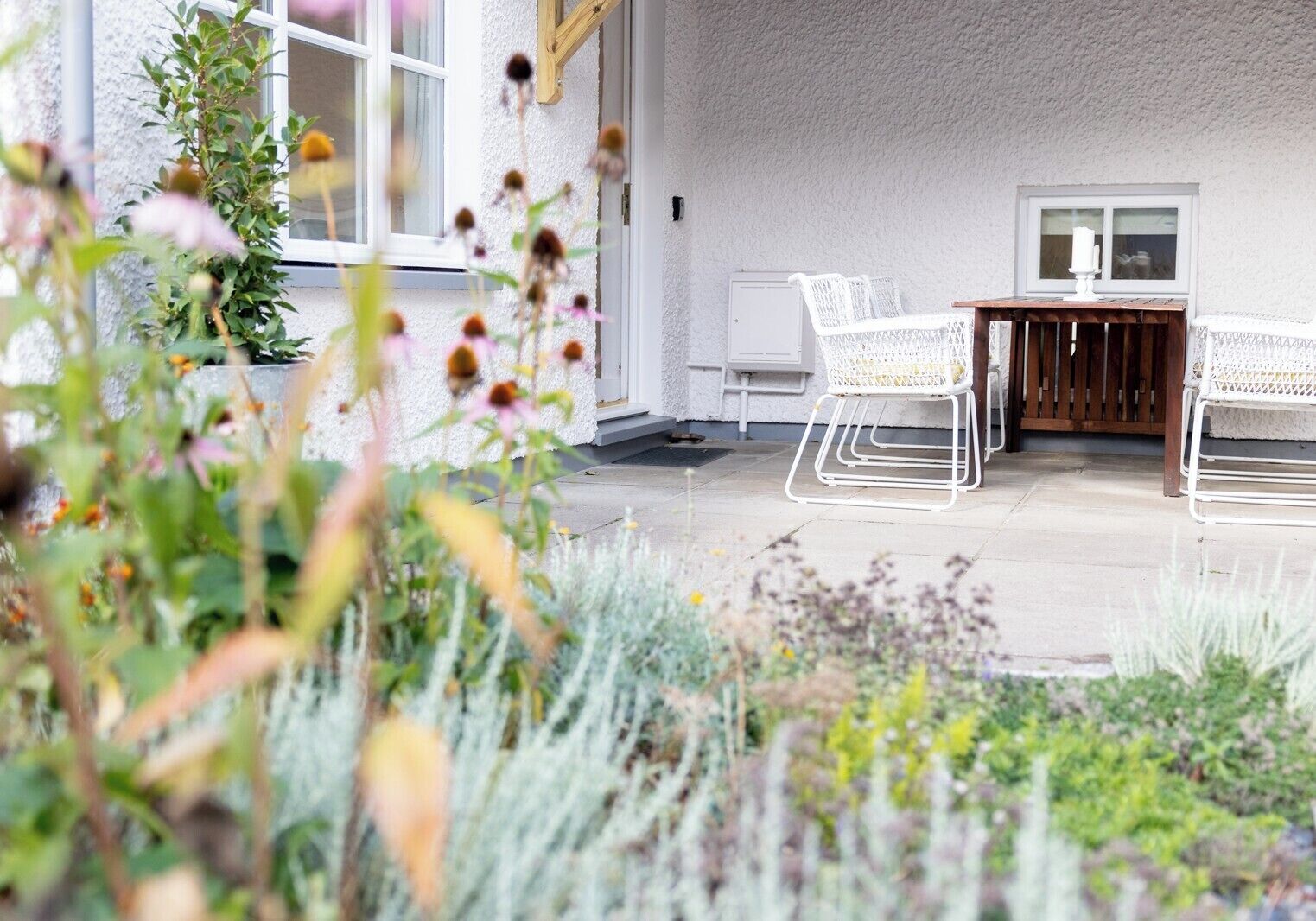 An outdoor patio area with white wicker chairs, a wooden table, and a white wall.