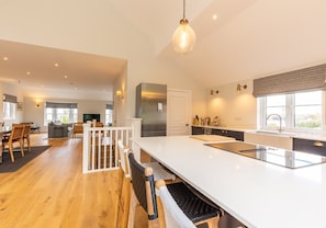 A spacious kitchen with a large island, modern appliances, and a dining area with wooden flooring and wicker furniture.