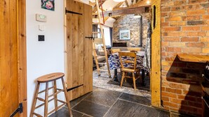 Un intérieur rustique avec des poutres apparentes, une cheminée en pierre et un coin repas comprenant une table et des chaises.