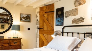 Une chambre à coucher avec un lit, une commode en bois et un mur en pierre.