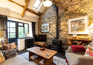 A cozy living room with a stone wall, a fireplace, a television, and a comfortable seating area. - A beautiful rustic cottage full of character and period features (Newport)