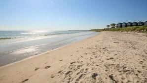 Una playa con huellas, cielo despejado y una fila de casas al pie de una colina cubierta de césped.