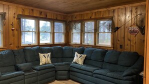 A cozy corner with a dark green sectional sofa, wooden walls, and large windows.