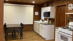 A wooden-paneled kitchen with white cabinets, a dining table with chairs, and a stove.