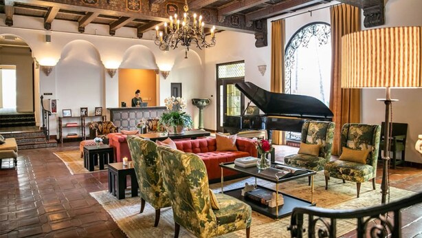 Een ruime lobby met een vleugelpiano, comfortabele zitplaatsen, een receptiebalie en een kroonluchter.