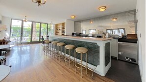 Een moderne keuken met een bar, grote ramen en een eethoek met tafel en stoelen.