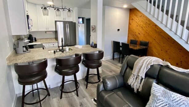 A modern kitchen with a central island, bar stools, a black leather sofa, and a wooden staircase. - 3BR Park Ave Townhome (Park City)