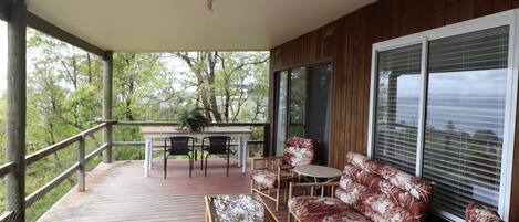 A covered outdoor deck with a table and chairs, a sofa, and a large window.