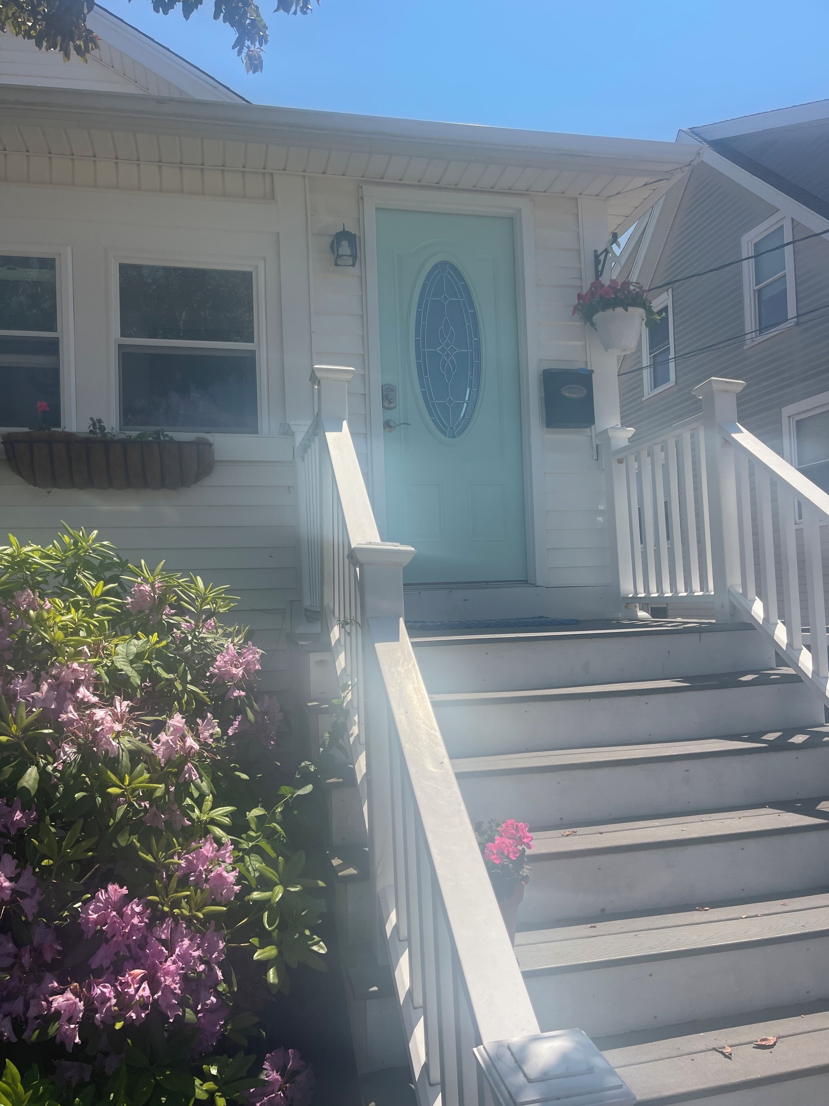 A house with a light green door, white railings, and steps leading to the front door.