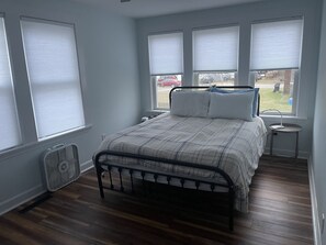 Cozy bedroom with a central bed, bedside tables, and lamps, offering a peaceful view of a residential area.