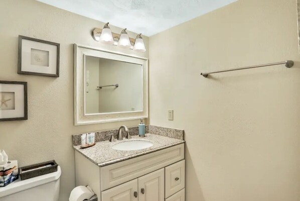 A bathroom with a sink, mirror, towel rack, framed pictures, and a toilet. - Amazing Ocean & River Views - 2BR Condo (Daytona Beach)