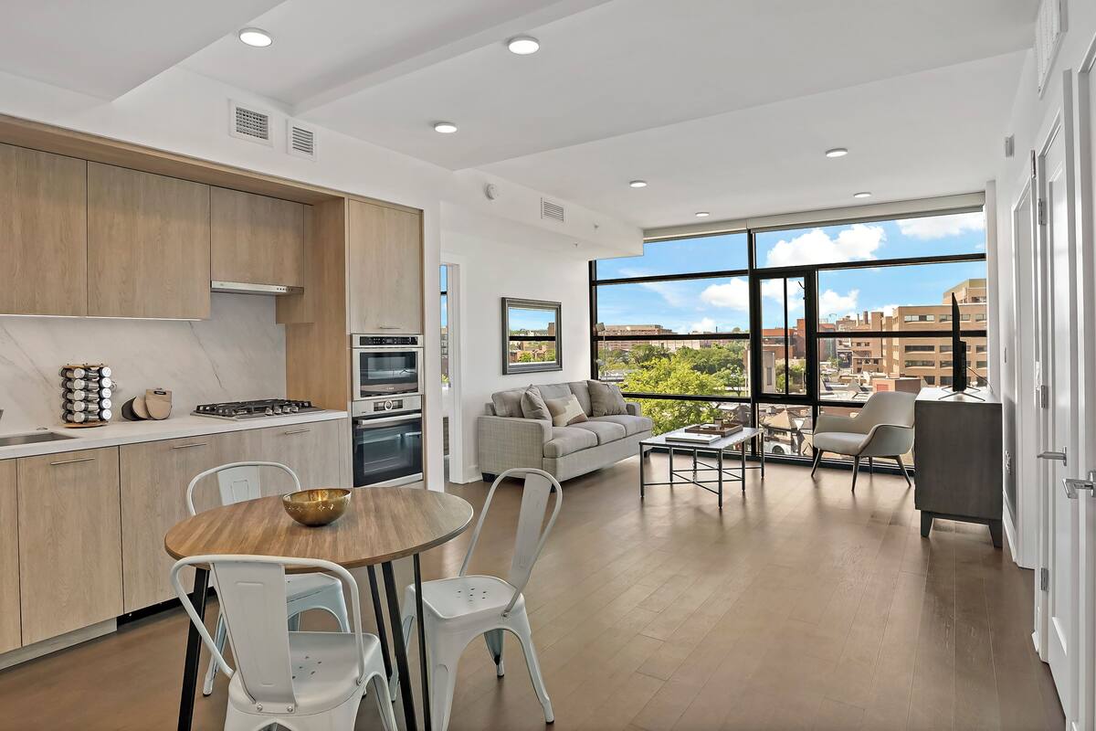 A modern kitchen with wooden cabinets, a dining area with a round table and chairs, and a living area with a sofa and a coffee table.