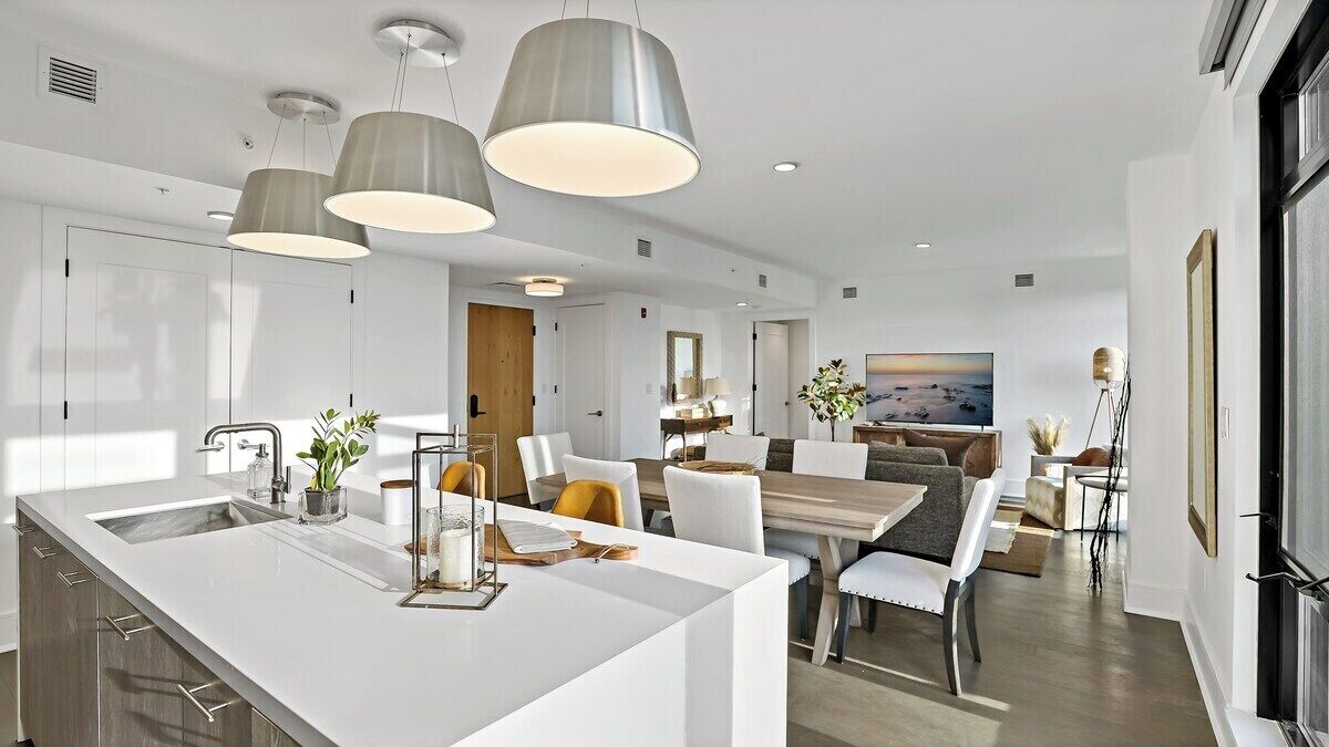 A modern kitchen with a central island, pendant lighting, and a dining area with a view of the city.
