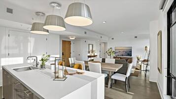 A modern kitchen with a central island, pendant lighting, and a dining area with a view of the city.