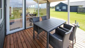 A covered outdoor area with a table and chairs, large sliding glass doors, and a view of a house in the background.