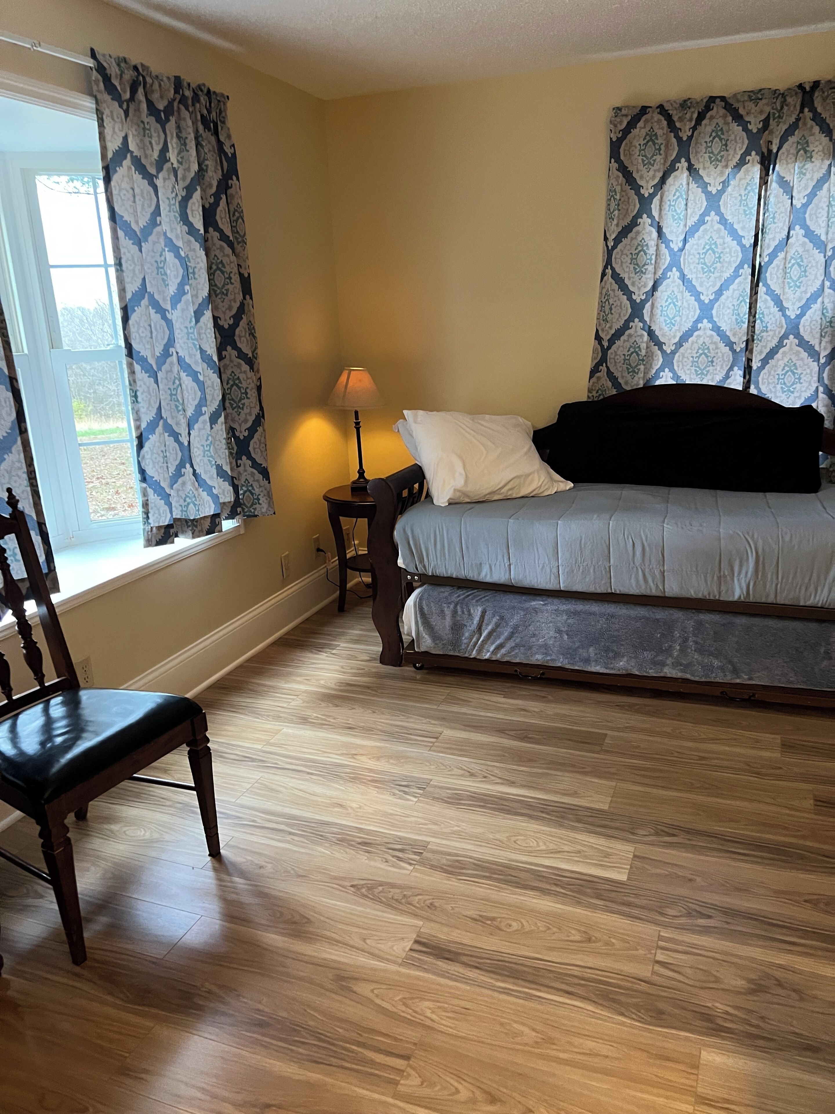 Une chambre à coucher avec un lit, une chaise, une table de chevet avec une lampe et des rideaux à motifs.