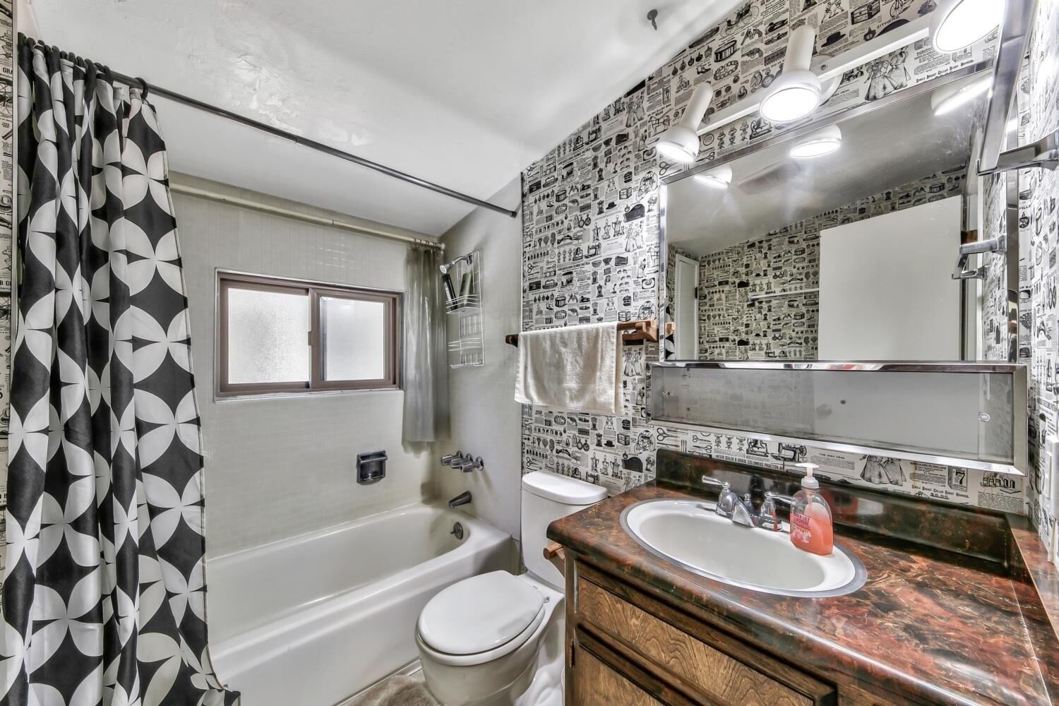 Une salle de bain équipée d’une baignoire, de toilettes et d’un lavabo. Les murs sont décorés d’un motif composé d’illustrations en noir et blanc.