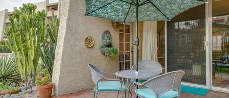 A patio with a table and chairs, a patterned umbrella, and a cactus.