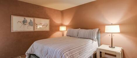 A bedroom with a bed, two bedside lamps, a nightstand, and two framed pictures on the wall.