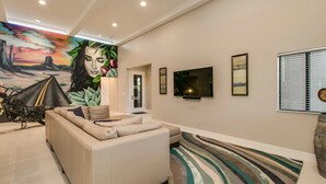 Een moderne woonkamer met een bank, een televisie en een muurschildering.