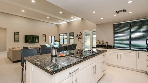 Een moderne keuken met een groot eiland, witte kastjes, en een zithoek met een grijze bank en stoelen.