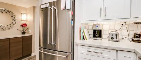 A modern kitchen with stainless steel appliances, white cabinetry, and a coffee maker on the counter.