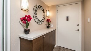 A hallway with a white door, a wooden cabinet, and two potted red flowers on a white countertop. - Cozy 2-bdrm Condo in Heart of Old Town Scottsdale! (Scottsdale)
